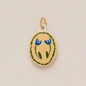 Detail of oval ceramic charm with blue floral pattern and gold jump ring attachment