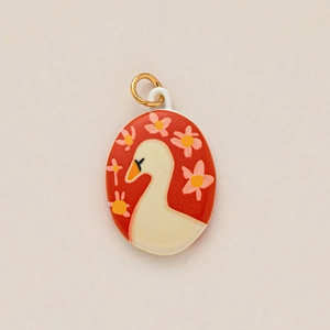 Detailed close-up of a red enamel oval pendant featuring a white swan and floral motifs