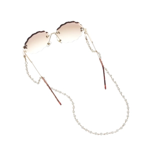 Détail de lunettes de soleil sans monture avec bords coquillage et chaîne en perles blanches