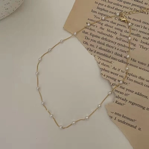 Minimalist gold chain necklace with round pearls displayed on vintage book pages