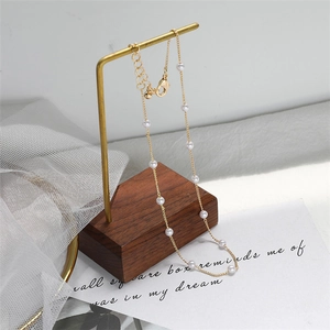 Detail of delicate gold pearl necklace on minimalist brass stand with soft mesh background