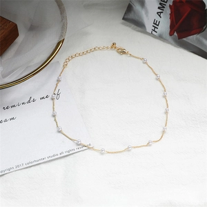 Close-up of golden pearl anklet with adjustable lobster clasp on elegant white fabric