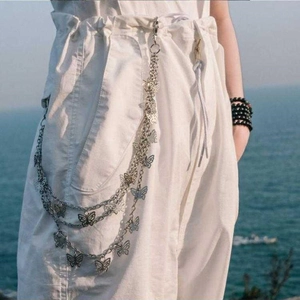 Macro detail of layered silver metal butterfly waist chain on white trousers