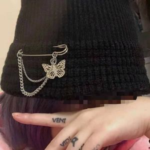 Detail of black knit beanie with silver double chains and butterfly pin accessory