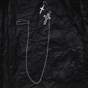 Détail d'une broche punk argentée avec deux croix et épingles sur fond noir froissé