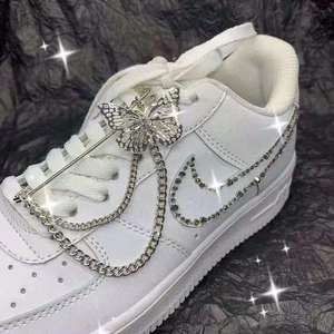 Detailed macro view of silver butterfly pin and double chain on white sneaker side