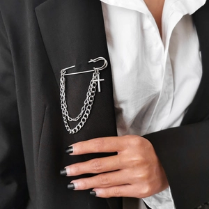 Detail of silver punk style safety pin brooch with layered chains and cross on black blazer