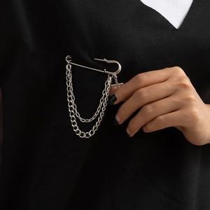 Detail of silver punk cross brooch with metal chains on a black V-neck garment
