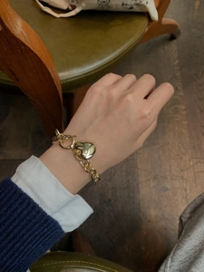 Dettaglio del bracciale a catena dorata con cuore e chiusura a T su polso femminile