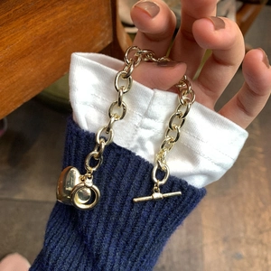 Dettaglio di un bracciale dorato con ciondolo a cuore e chiusura a ginocchiera sulla manica