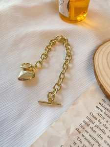 Dettaglio del bracciale con ciondolo a cuore dorato e chiusura a T su sfondo bianco