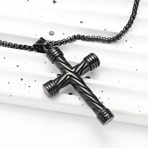 Vue macro d'un pendentif croix noir en acier inoxydable avec textures spirales et chaîne box