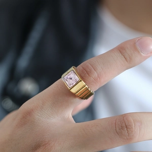 Détail d'une bague avec pierre rose carrée et anneau doré texturé sur le doigt