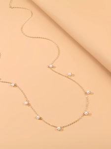 Détail d'une chaîne de taille dorée ornée de perles sur un fond beige minimaliste