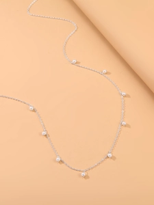Vue détaillée d'une chaîne argentée avec perles blanches sur fond orange chaud