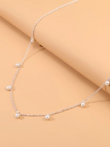 Détail de la chaîne de taille argentée avec perles blanches sur fond rose doux