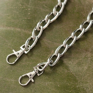 Close-up of dual silver metal trouser chains with lobster clasps on green leather