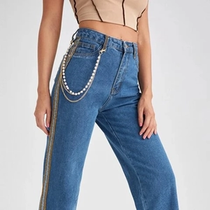 Détail de chaînes dorées multicouches et breloques en perles sur un jean bleu taille haute