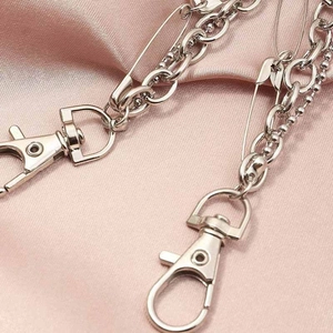 Multi-layer silver metal pants chain with bear charms and safety pin on pink satin background