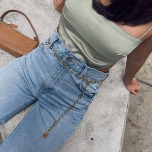 Detail of trendy gold alloy waist chain with round pendant worn over light blue jeans