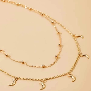 Détail d'une chaîne dorée à deux rangs avec perles et pendentifs en forme de lune