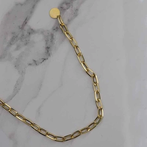 Detailed close-up of golden paperclip chain necklace with a round pendant on marble background