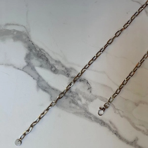 Detailed macro view of silver alloy chain with lobster clasp and round pendant on marble