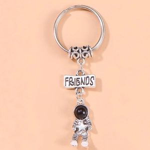Silver astronaut keychain with Friends engraved plaque on a minimalist orange background