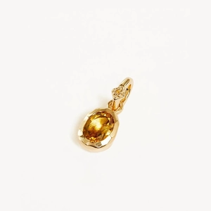 Macro detail of oval cut yellow gemstone pendant with gold-plated setting and diamond accent