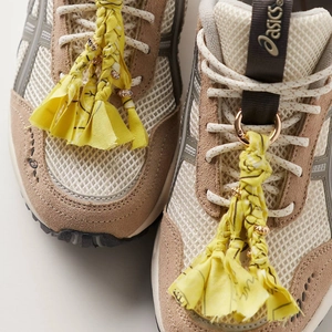 Detail of colorful tassel charm and gold beads on a mesh sneaker with beige suede