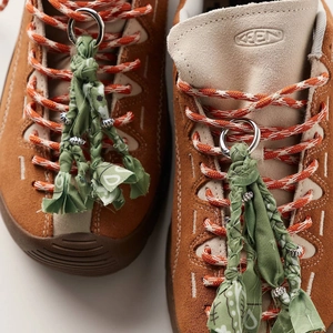 Close-up of green tassel pendant with silver beads on orange woven shoelaces