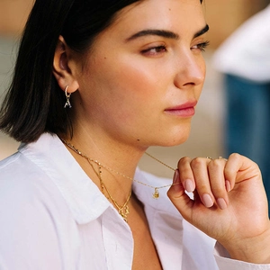 Detailopname van een model met gouden letter A-oorring en gelaagde roestvrijstalen kettingen