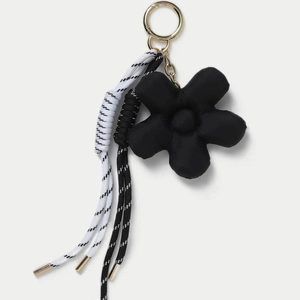 Detail of elegant black five-petal flower bag charm with gold ring and braided ropes