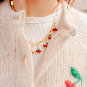 Gros plan du collier pendentif cerise plaqué or 18K sur un cardigan en maille beige