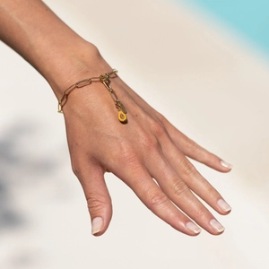 Gros plan du bracelet trombone doré avec breloque papaye en émail sur un poignet