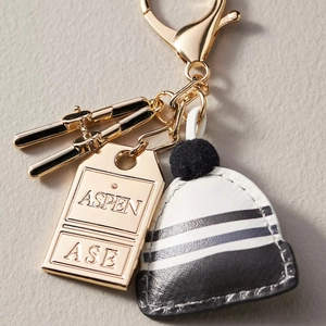 Close-up of golden ski charms and striped knit hat keychain with Aspen engraved tag