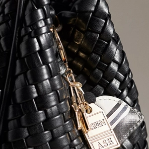Close-up of black woven leather texture and gold metal tag pendant on a pickleball bag