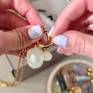 Detailed close-up of golden necklace featuring raw yellow stone and white jade charms