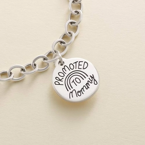 Macro detail of silver stainless steel pendant engraved with Promoted To Mommy text