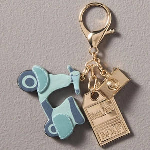 Detailopname van de gouden sleutelhanger met blauwe scooter en Milan gegraveerd label