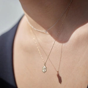 Detailopname van gelaagde 18K vergulde kettingen met vintage roos-reliëfhanger op een model