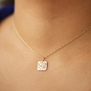 Detailopname van een vierkante gouden hanger met gegraveerde bloemen en een gedraaide ketting