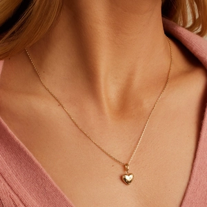 Close-up van een gouden hartjesketting met stergravure gedragen door een model