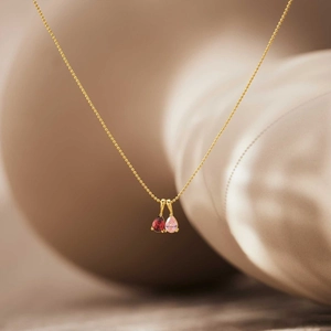 Detailed shot of double pear-shaped red and pink stones on a gold bead chain necklace