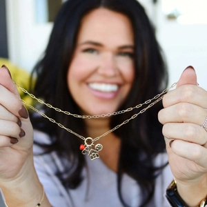 Detail of a gold paperclip chain necklace with heart, house, and smiley face charms