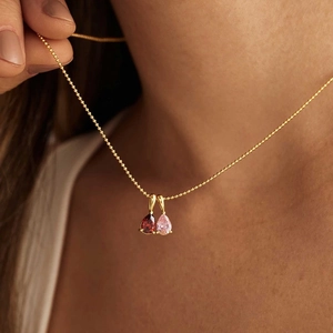 Close-up of dual teardrop birthstone pendants on a gold beaded chain worn by a model