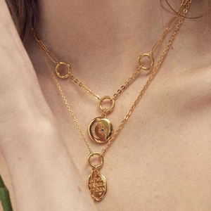 Detail of layered 18K gold necklaces with celestial sun moon pendant and vintage coin charm