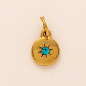 Detailed macro of golden matte round pendant with sunburst star and blue gemstone