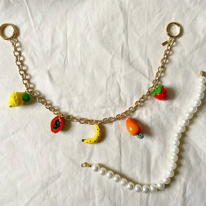 Détail d'une chaîne plaquée or 14K avec breloques fruits en émail sur lin de couleur beige