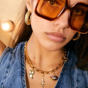 Close-up of gold chain heart necklace and textured hoop earrings on a fashion model